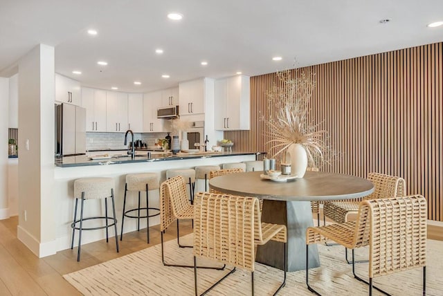 kitchen featuring a peninsula, freestanding refrigerator, light wood-style floors, stainless steel microwave, and a kitchen breakfast bar