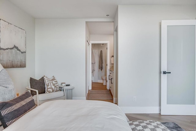 bedroom with ensuite bath, wood finished floors, and baseboards