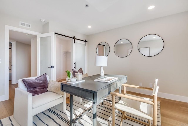 office space with a barn door, recessed lighting, visible vents, and light wood-type flooring