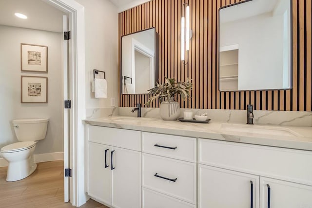 full bathroom with baseboards, double vanity, wood finished floors, toilet, and recessed lighting