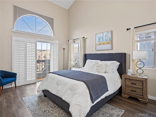 bedroom with multiple windows, a towering ceiling, and dark wood-style flooring