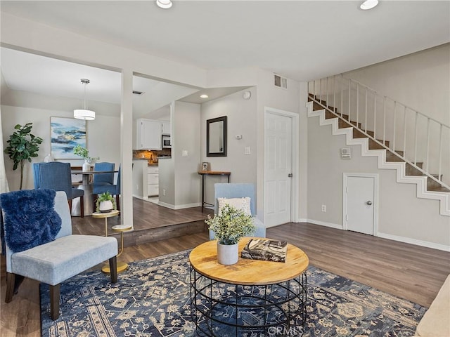 living room featuring stairway, wood finished floors, visible vents, and baseboards