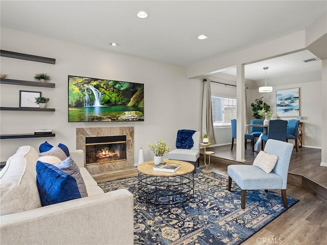 living area with wood finished floors, visible vents, baseboards, a premium fireplace, and recessed lighting