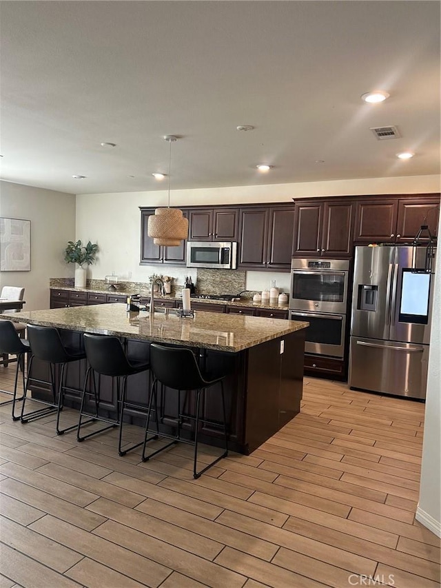 kitchen featuring visible vents, light wood-style flooring, dark stone countertops, a kitchen breakfast bar, and appliances with stainless steel finishes