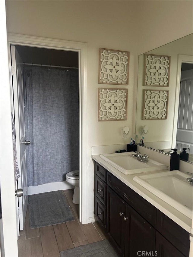 full bath featuring toilet, a sink, curtained shower, double vanity, and wood tiled floor