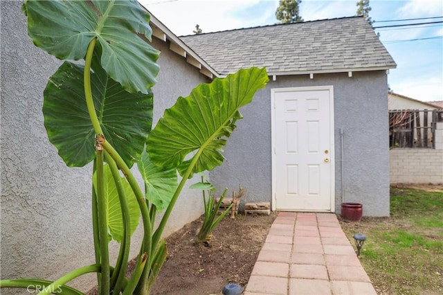 doorway to property with a shingled roof, fence, and stucco siding