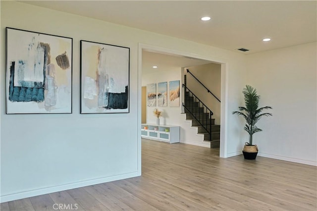 empty room featuring recessed lighting, light wood-type flooring, stairs, and baseboards