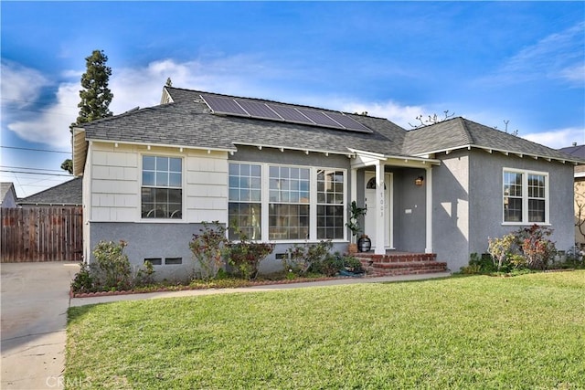 view of front of home featuring fence, solar panels, a shingled roof, stucco siding, and a front lawn