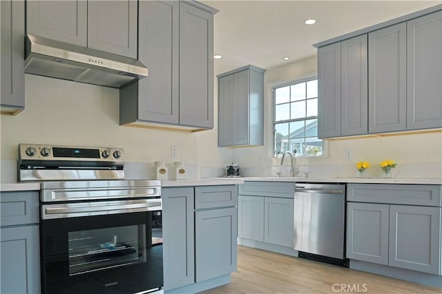 kitchen with light countertops, appliances with stainless steel finishes, under cabinet range hood, and gray cabinetry