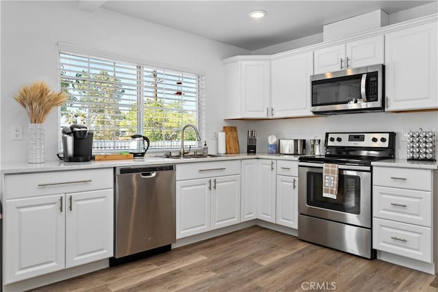 kitchen with light countertops, light wood-style flooring, appliances with stainless steel finishes, white cabinets, and a sink