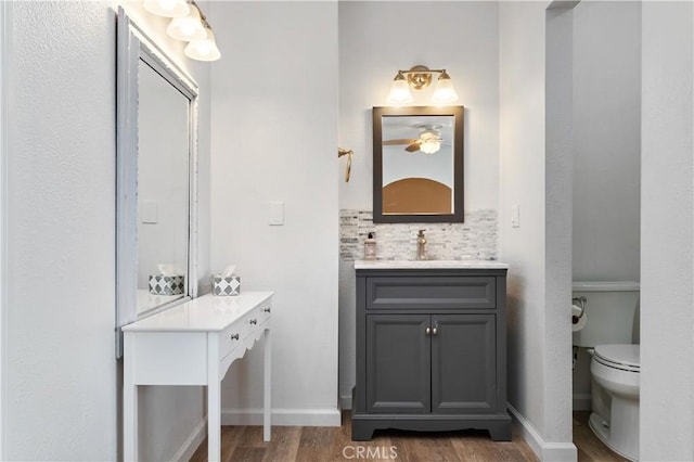 bathroom featuring toilet, tasteful backsplash, wood finished floors, baseboards, and vanity