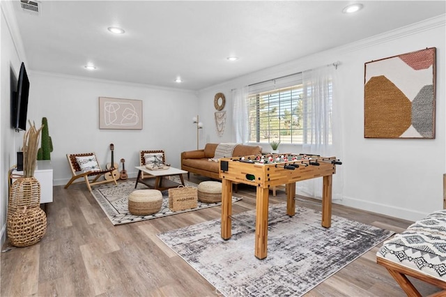 living area featuring baseboards, wood finished floors, visible vents, and ornamental molding