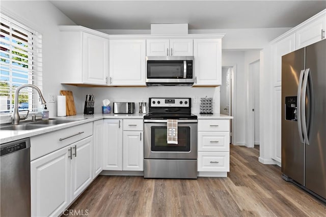 kitchen featuring light countertops, appliances with stainless steel finishes, wood finished floors, white cabinetry, and a sink