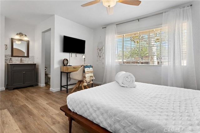 bedroom with ensuite bath, a ceiling fan, baseboards, and wood finished floors