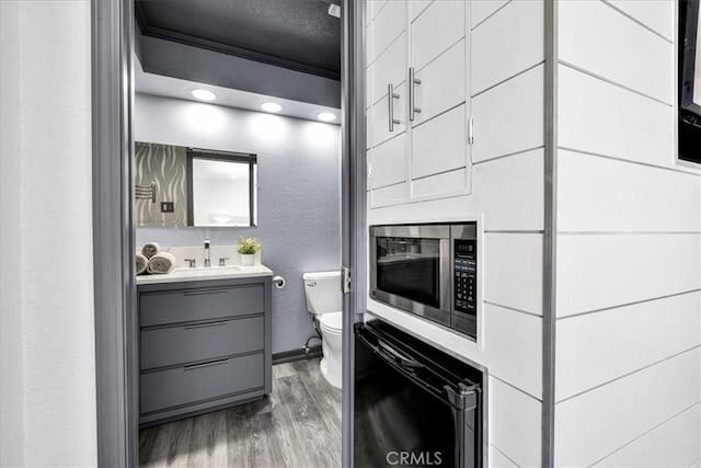 bathroom featuring toilet, wood finished floors, ornamental molding, a textured wall, and vanity