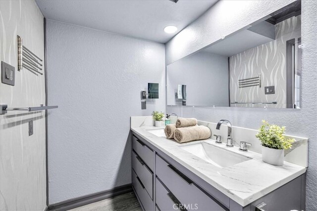 bathroom featuring wood finished floors, vanity, baseboards, and a textured wall