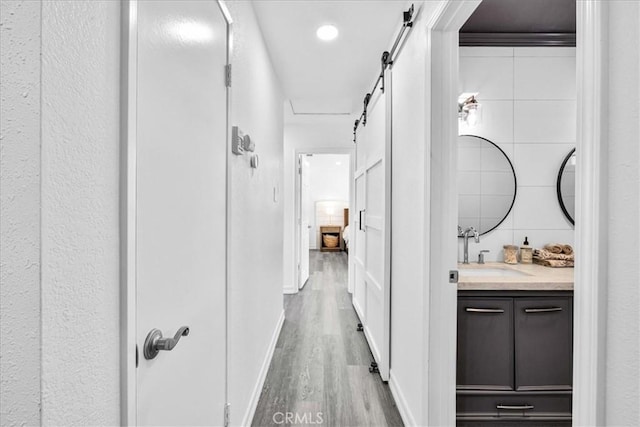 hallway with a barn door, wood finished floors, baseboards, and a sink