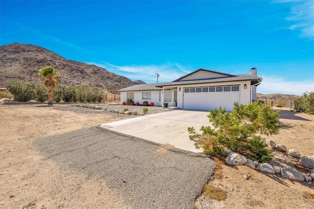 single story home featuring a chimney, a mountain view, driveway, and an attached garage