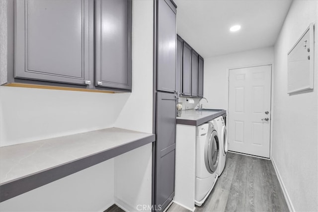 washroom with wood finished floors, baseboards, cabinet space, a sink, and washing machine and dryer