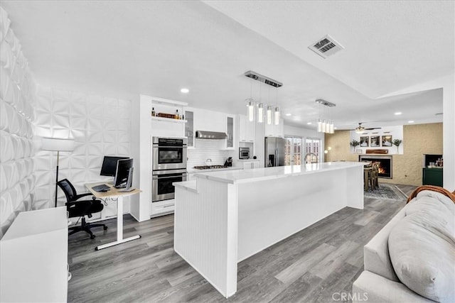 kitchen with white cabinetry, open floor plan, stainless steel appliances, and a lit fireplace