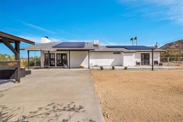 rear view of house with fence, roof mounted solar panels, stucco siding, french doors, and a patio area