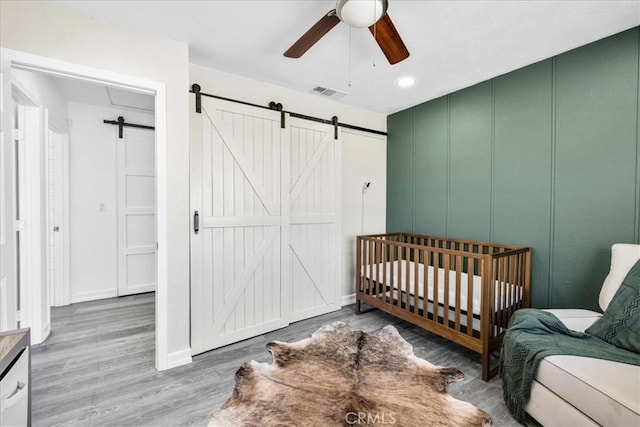 bedroom with visible vents, a decorative wall, a barn door, and wood finished floors