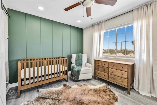 bedroom with recessed lighting, a nursery area, wood finished floors, and a ceiling fan