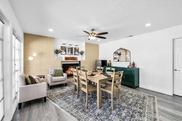 dining space with a ceiling fan, wood finished floors, baseboards, recessed lighting, and a lit fireplace