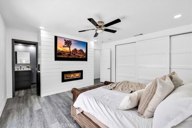 bedroom with wood finished floors, visible vents, recessed lighting, a fireplace, and a closet