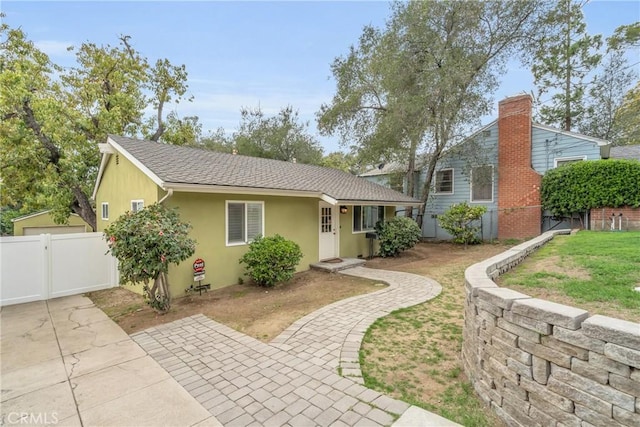 view of front of home with a front yard, a gate, fence, a shingled roof, and stucco siding