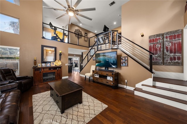 living area featuring stairs, a glass covered fireplace, wood finished floors, and visible vents