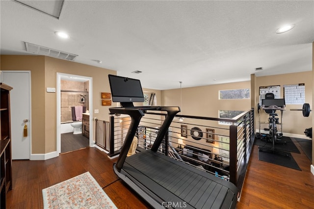 exercise room featuring visible vents, wood-type flooring, a textured ceiling, and baseboards