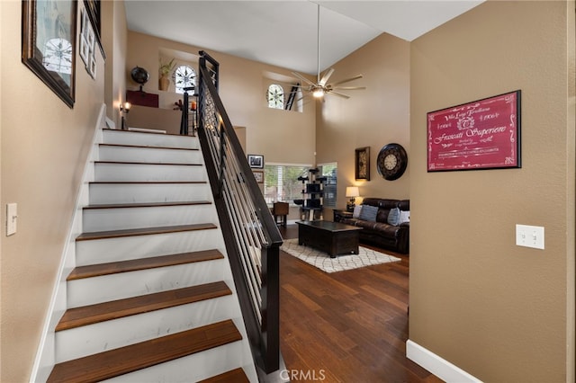 stairway featuring baseboards, a high ceiling, ceiling fan, and wood finished floors