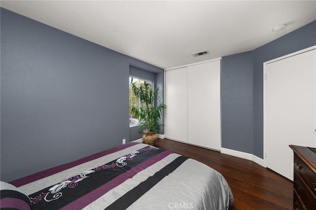 bedroom with wood finished floors, visible vents, a closet, and baseboards