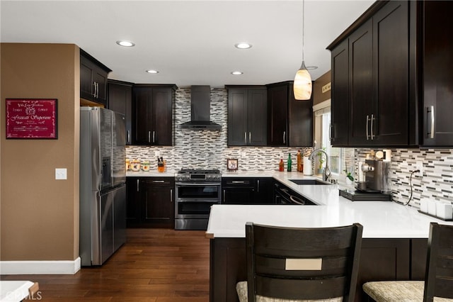 kitchen with a sink, stainless steel appliances, a peninsula, wall chimney exhaust hood, and light countertops