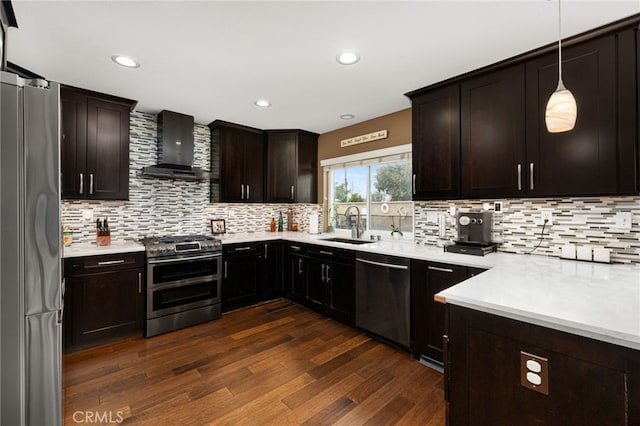 kitchen with wall chimney range hood, dark wood finished floors, light countertops, stainless steel appliances, and a sink