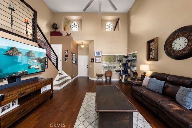 living area with stairway, a towering ceiling, baseboards, and wood finished floors