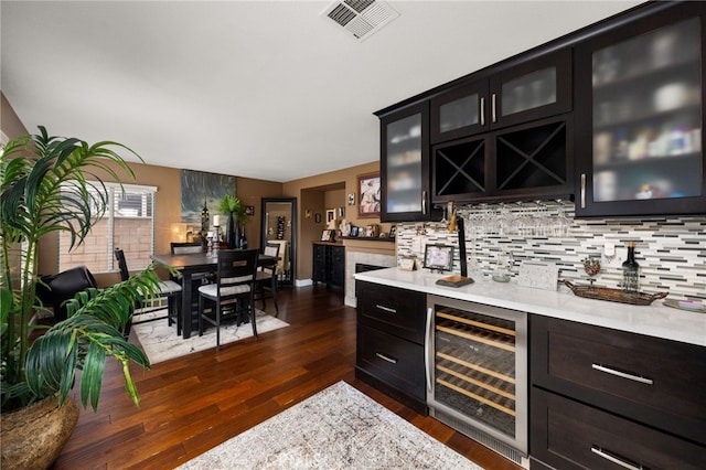 bar with visible vents, dark wood-type flooring, beverage cooler, tasteful backsplash, and indoor wet bar