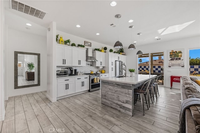 kitchen with visible vents, a kitchen island with sink, stainless steel appliances, decorative backsplash, and wall chimney exhaust hood