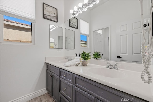 full bath featuring double vanity, wood finished floors, baseboards, and a sink