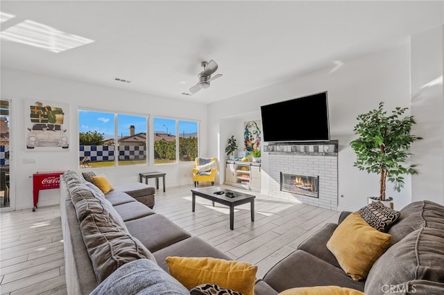 living room with visible vents, a brick fireplace, baseboards, wood finished floors, and a ceiling fan