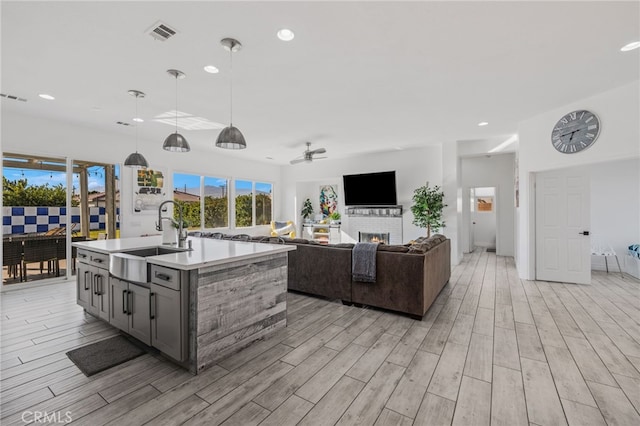 kitchen featuring visible vents, wood finish floors, light countertops, a warm lit fireplace, and a sink