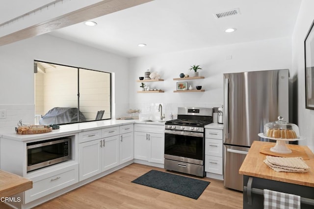 kitchen featuring light wood finished floors, visible vents, tasteful backsplash, appliances with stainless steel finishes, and a sink