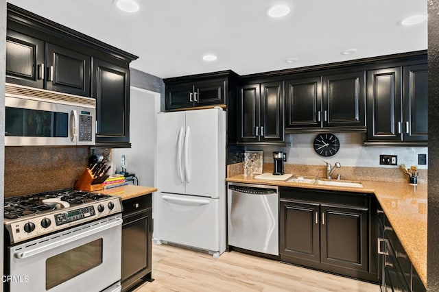 kitchen featuring dark cabinetry, recessed lighting, a sink, light wood-style floors, and appliances with stainless steel finishes