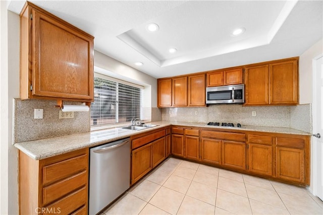 kitchen with a raised ceiling, brown cabinets, appliances with stainless steel finishes, and a sink