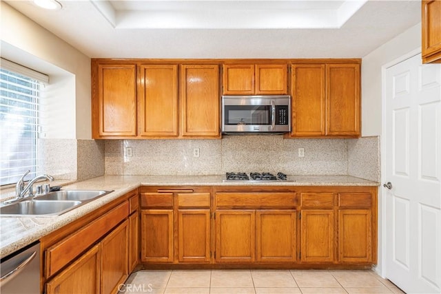 kitchen with light countertops, brown cabinetry, appliances with stainless steel finishes, and a sink