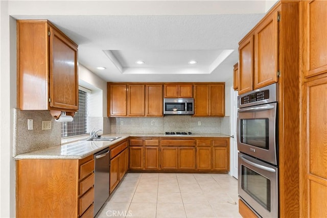 kitchen with brown cabinetry, backsplash, appliances with stainless steel finishes, and a tray ceiling