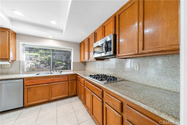 kitchen with brown cabinets, stainless steel appliances, a raised ceiling, and a sink