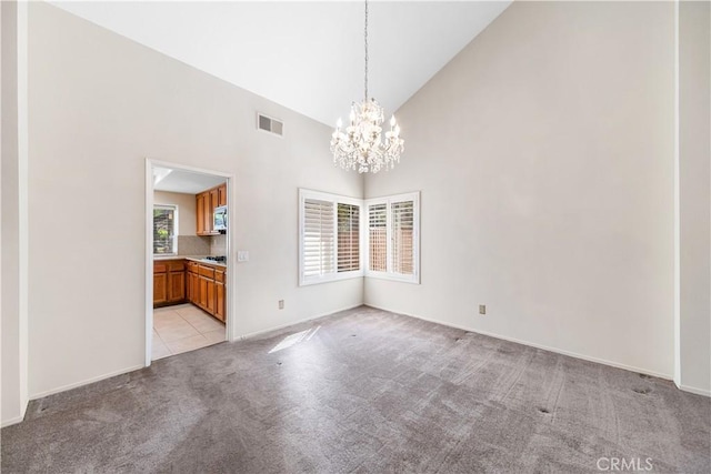 unfurnished dining area featuring visible vents, baseboards, light colored carpet, an inviting chandelier, and high vaulted ceiling