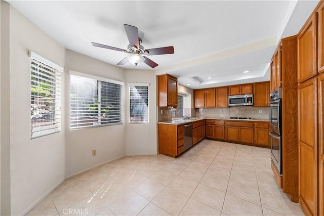 kitchen featuring light countertops, a tray ceiling, decorative backsplash, brown cabinets, and appliances with stainless steel finishes